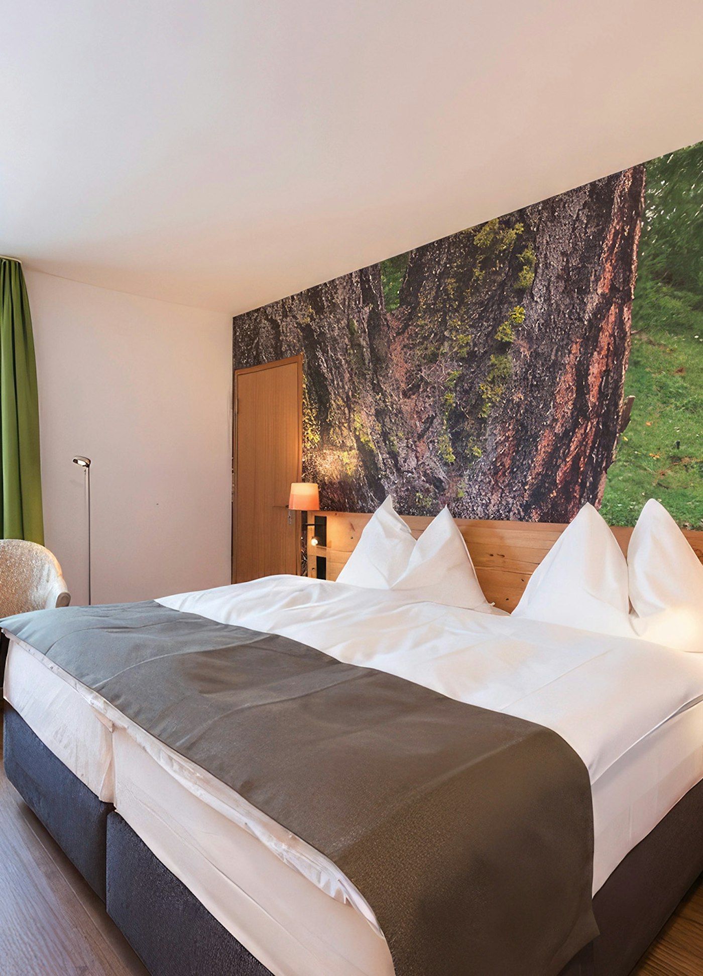 Doppelbett in weiss mit brauner Tagesdecke darauf, im Hintergrund Foto mit Rinde einer Lärche