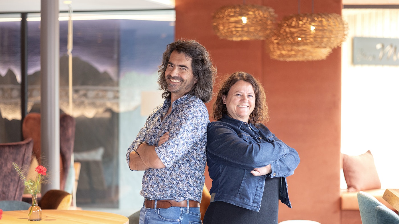 Sonja und Andrea Isepponi stehen im Loungebereich Rücken an Rücken aneinander und lachen in die Kamera