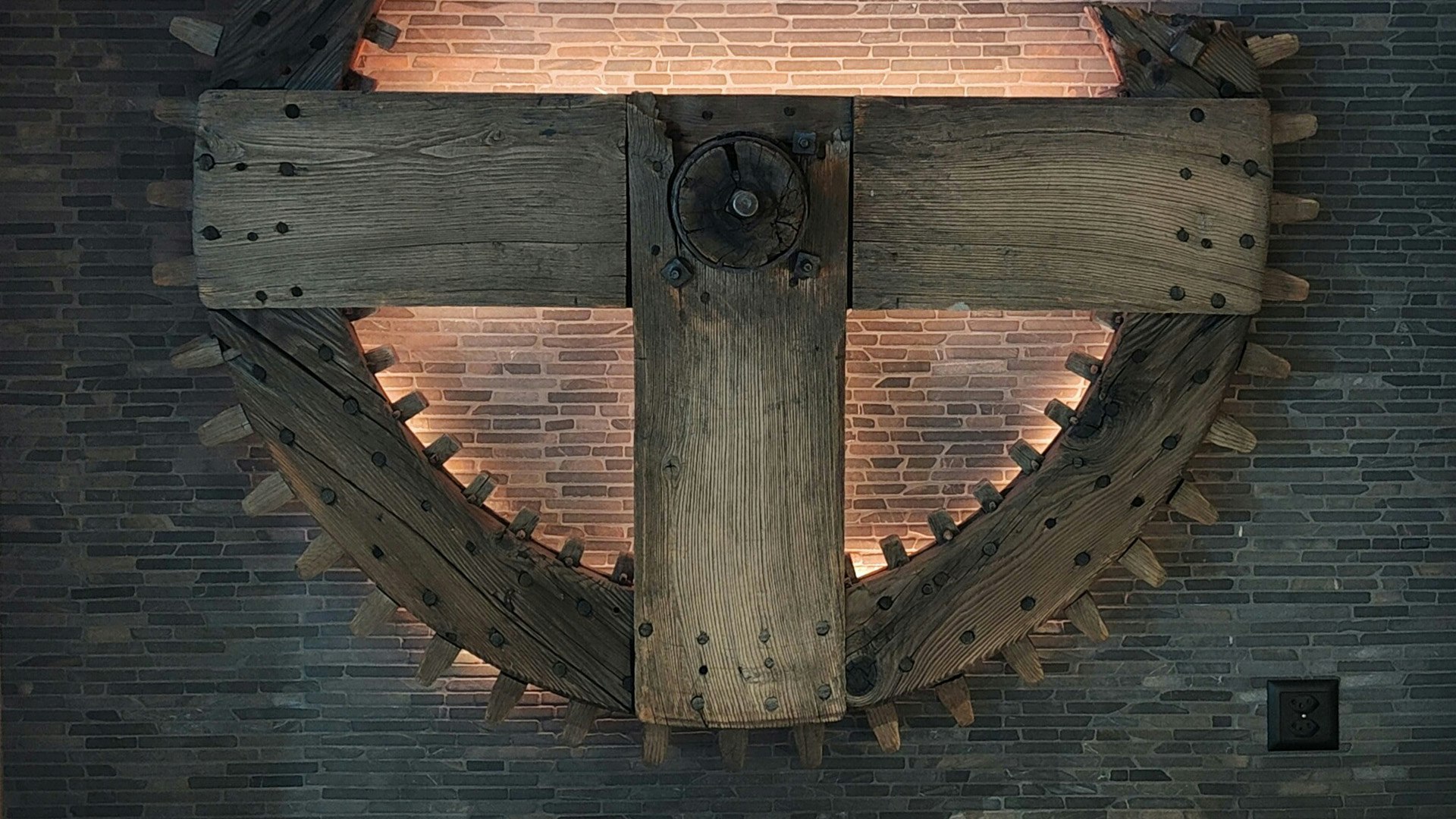 Old wooden mill wheel hangs on the wall and is lit from behind