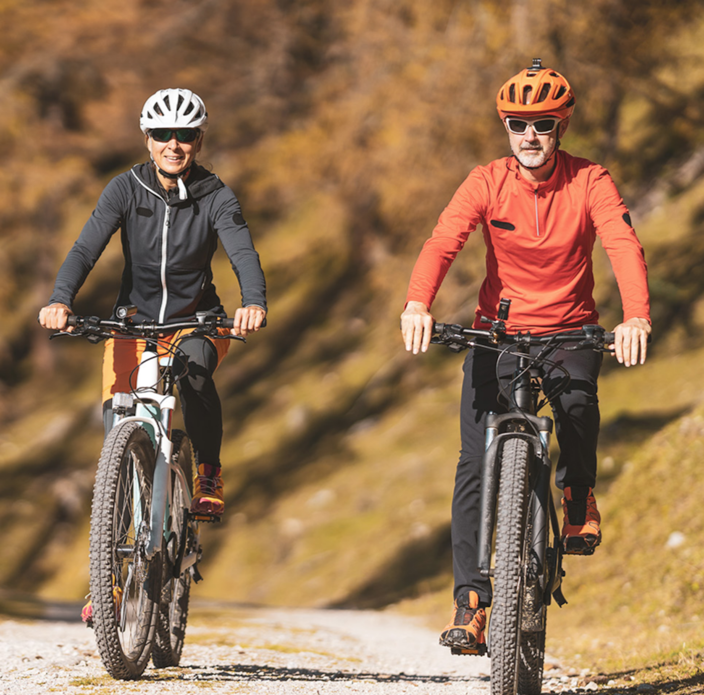 Zwei Fahrradfahrer mit Bike, links Frau in schwarzem Outfit und recht Mann mit Orangerer Jacke und Helm mit schwarzen Hosen, Herbst,