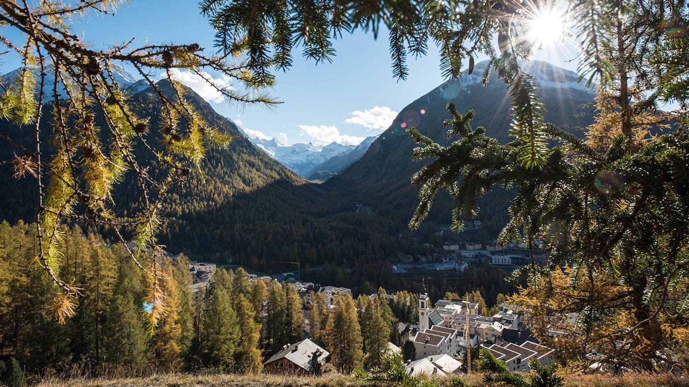 The village seen from above from a slope, view of the Rosegtal mountains and sunbeams in the background