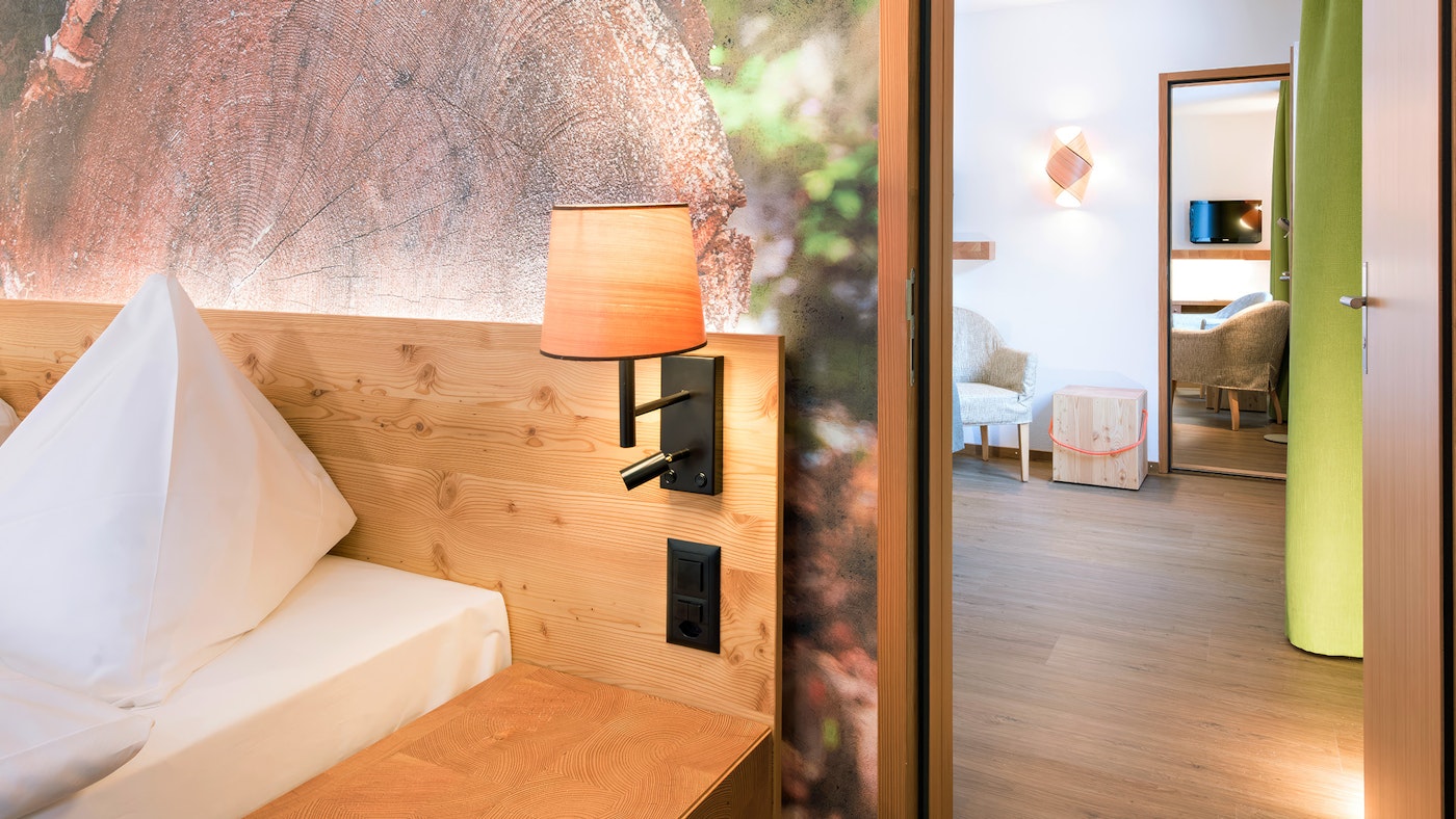 Durchgang zu anderem Zimmer mit Spiegel, Sessel und Holztisch, rechts Doppelbett mit Lampe