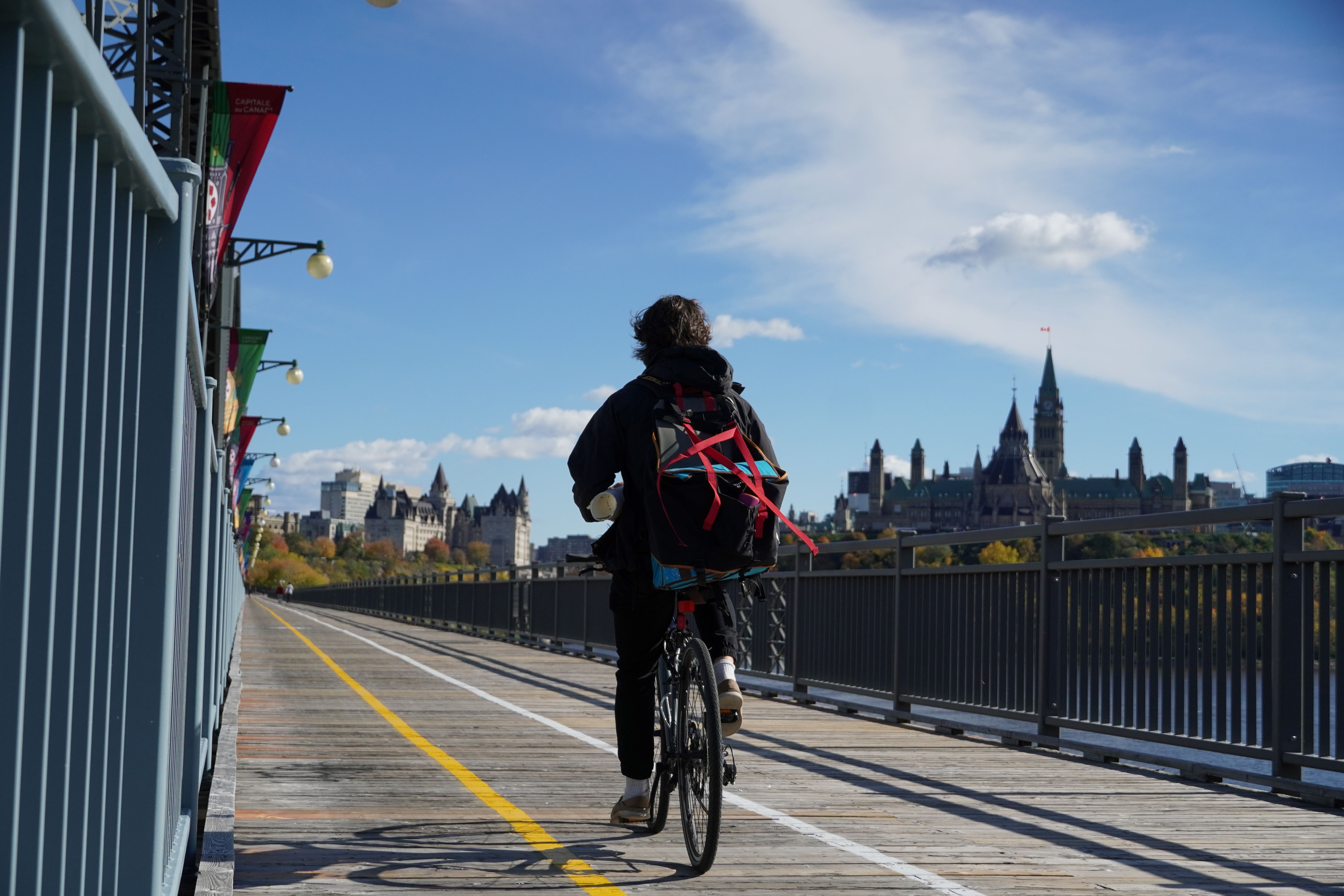 Cycliste sur un pont avec la Colline du Parlement (Ottawa) en arrière plan