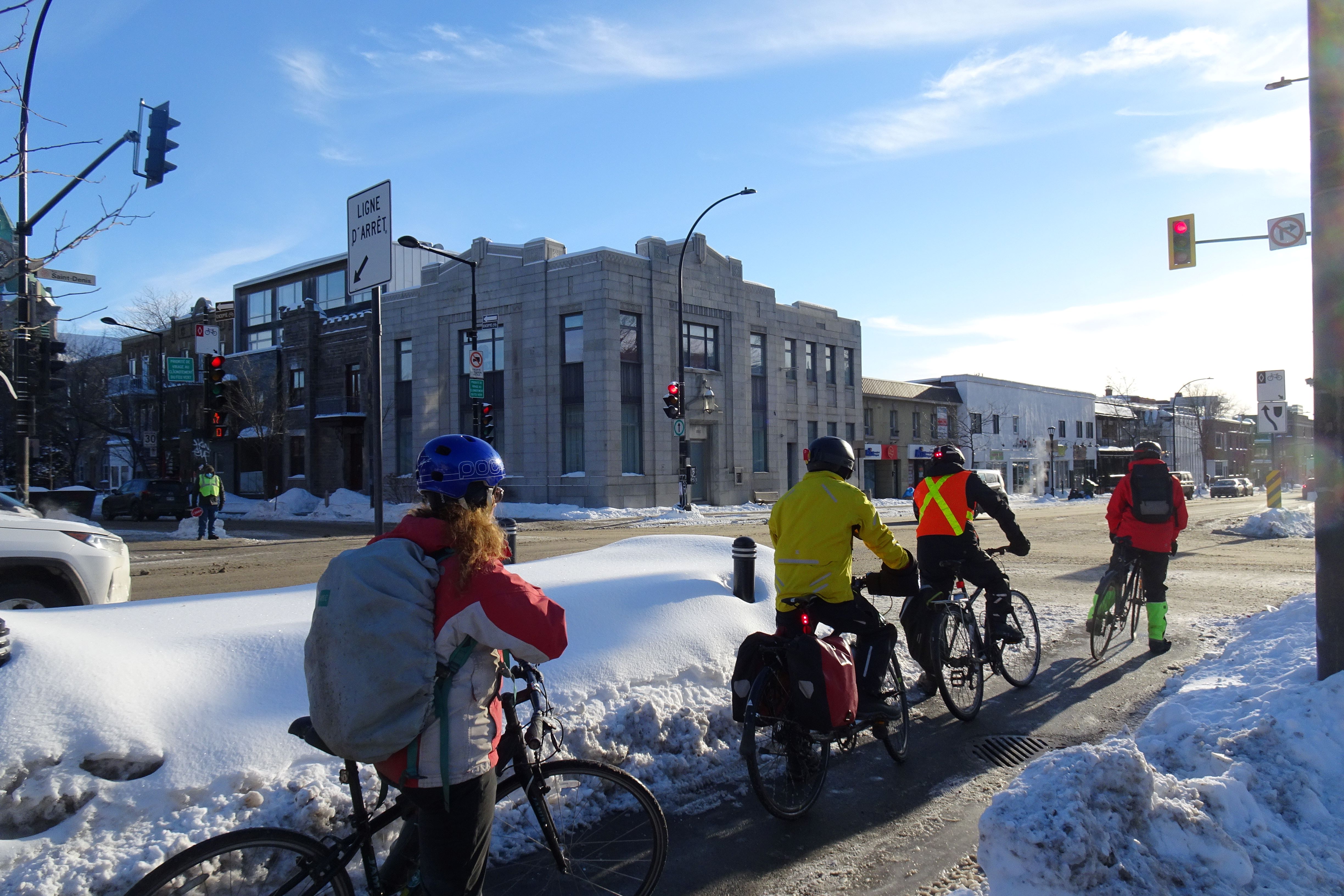 Four urban cyclists waiting at a red light next to snowbanks