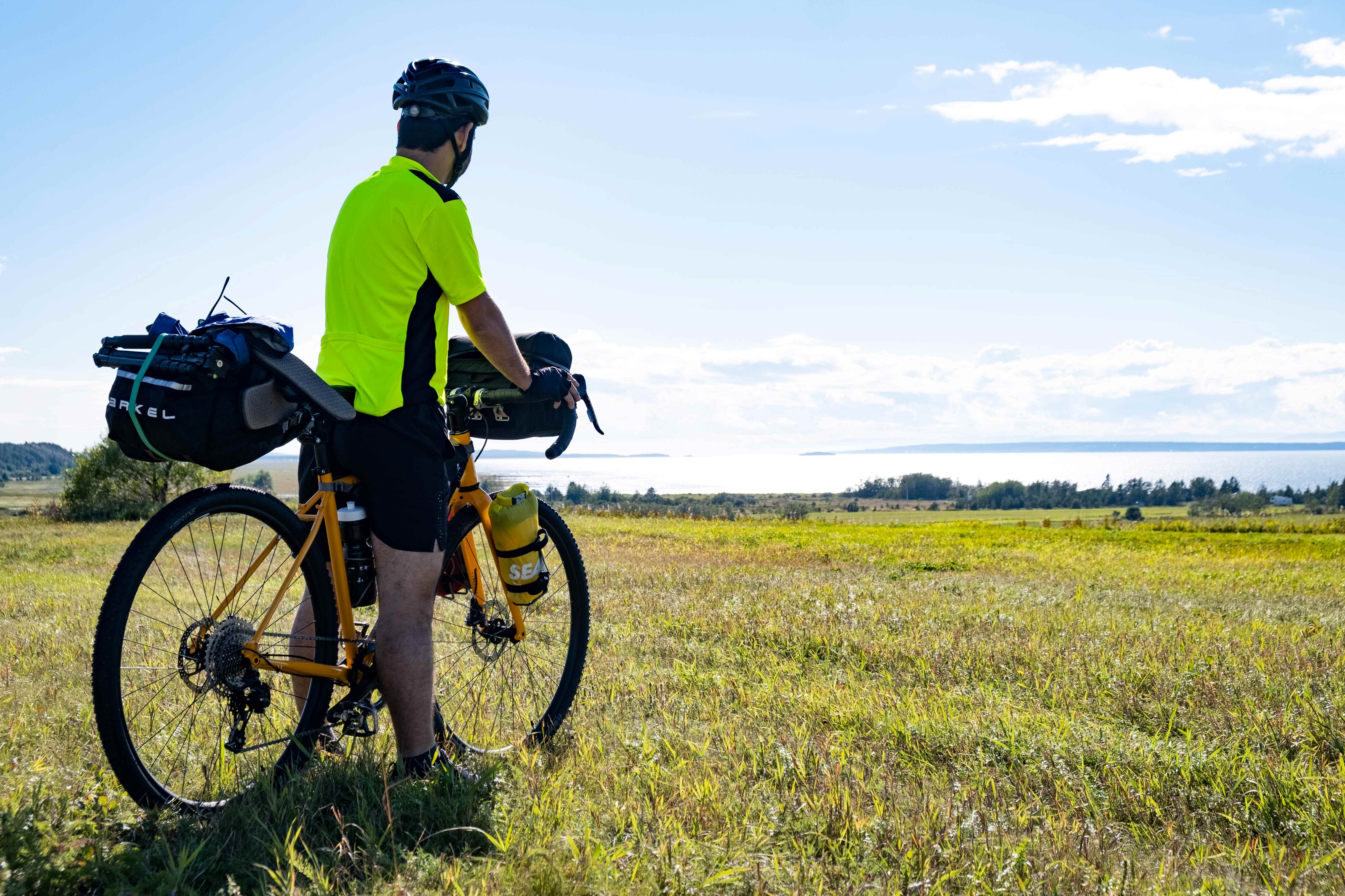 A cyclist in front of the Saint Lawrence River and a meadow in summer