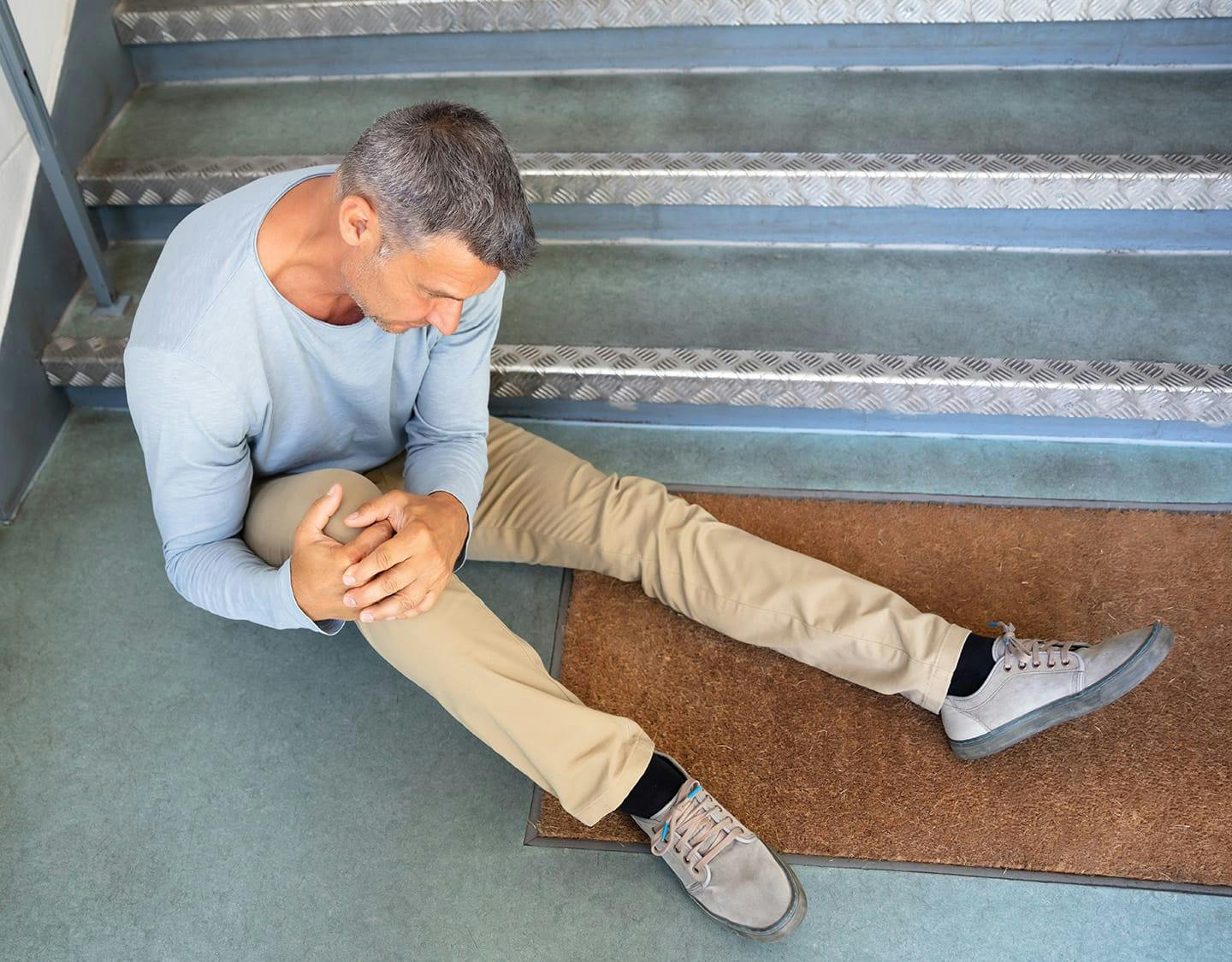 man sitting at bottom of stairs, holding his knee