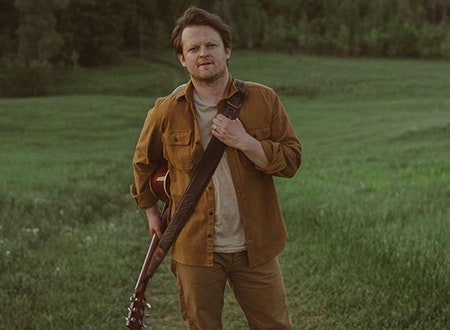 Mattie Leon standing in a field with his guitar.