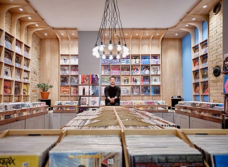 Tiny_Record_Shop_Trevor.jpg Owner in tiny record shop with crate of records on display: Cozy store interior with shelves of vinyl albums and proprietor standing in front of thier music collection.