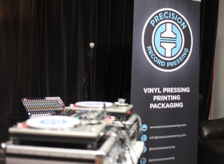 DJ turntable and set up in front of a Precision Record Pressing banner.