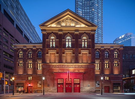 View of Massey Hall, Toronto: A historic concert venue with red-brick architecture, set against a bustling urban backdrop under a clear blue sky.