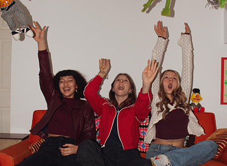 Thunder Queen band sitting on a couch joyfully throwing stuffed toy Muppets in the air.