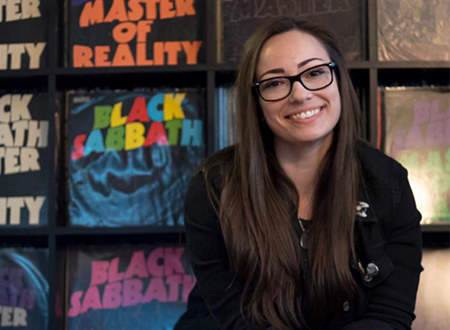 Jenn D'Eugenio sitting in front of a collection of Black Sabbath 'Master of Reality' vinyl records.