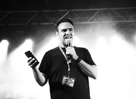 Pp7ruGOq-UpHereMarc-Etienne-Mongrain-11.png Up Here Festival founder Christian Pelletier speaking into a microphone onstage.