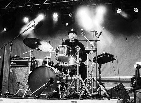 Member of the band Super Dirty Tough Work singing and drumming onstage.