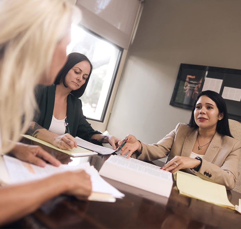 three women sitting around a table looking at documents