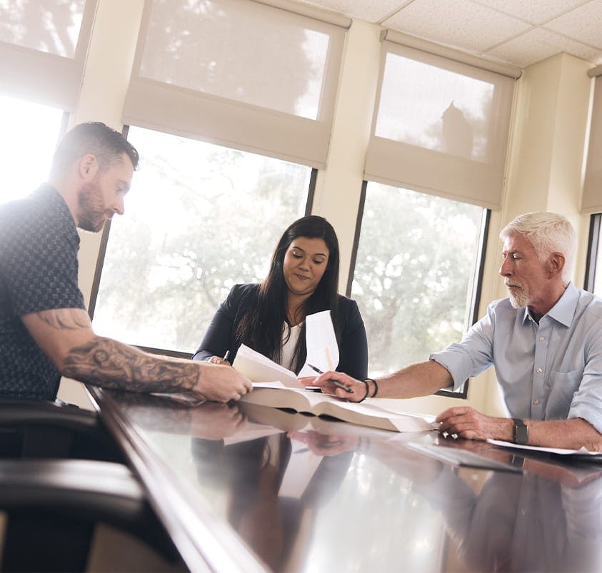 three people around a table looking at a book and documents