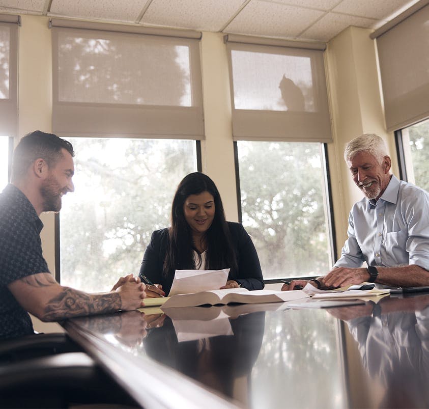 three people sitting at a table looking at documents
