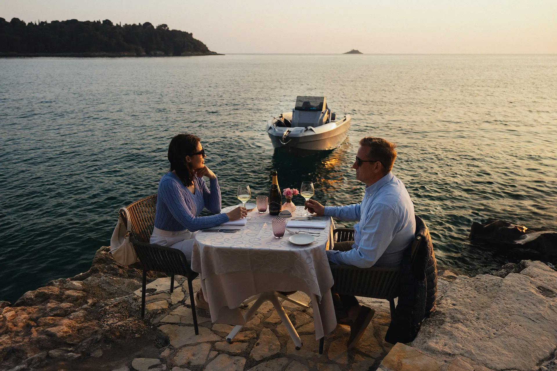 A couple having a romantic dinner at sunset with Hydra 530 Family Boat in the background