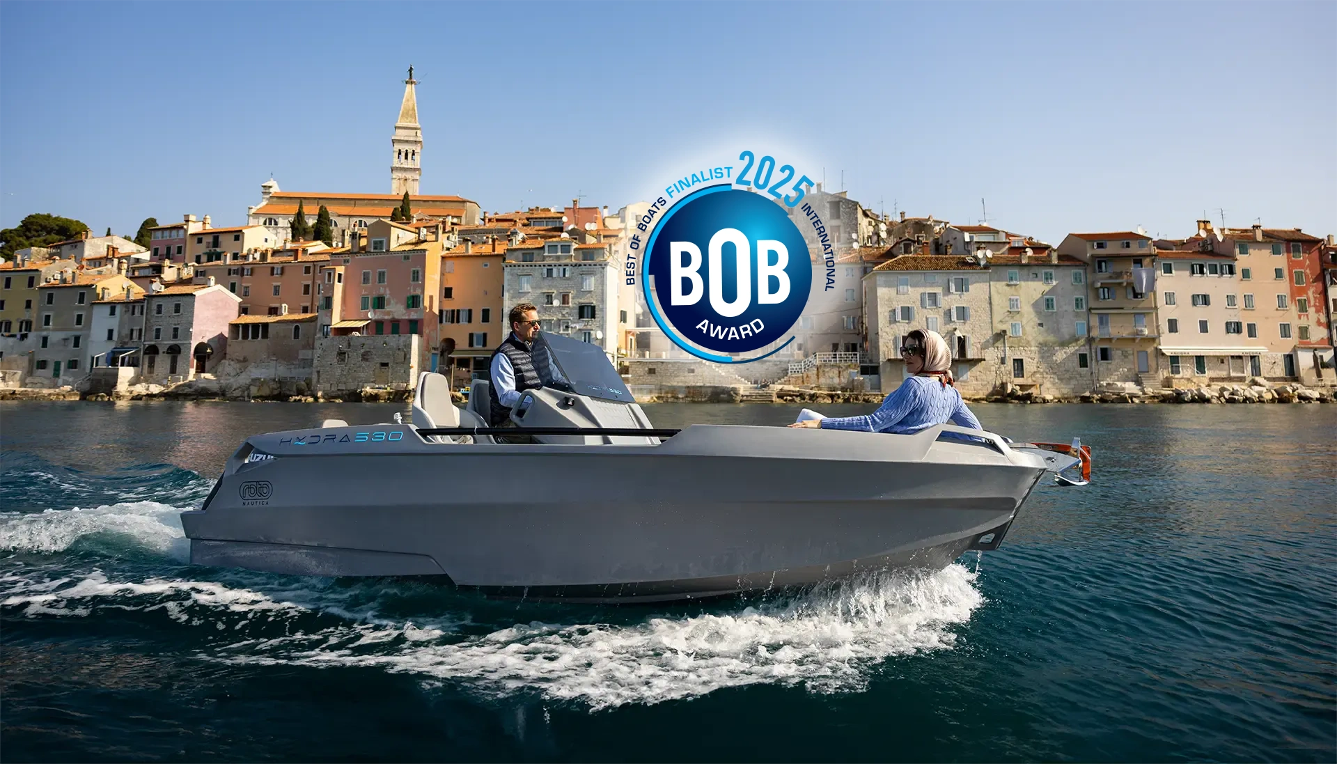 A man driving a Hydra 530 family boat across the water, heading out of a harbour.