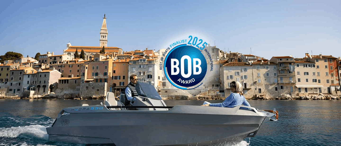 A man driving a Hydra 530 family boat across the water, heading out of a harbour.