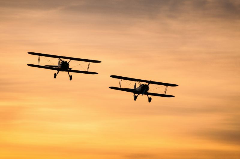 Biplanes flying through the sky at sunset