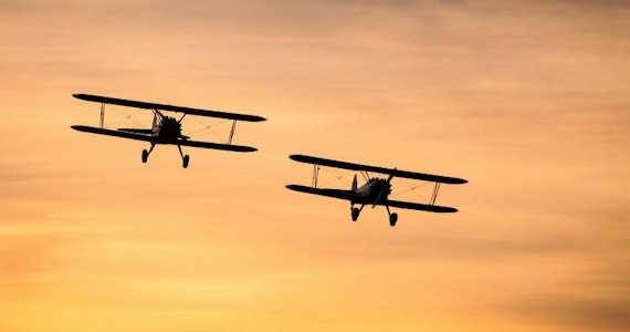 Biplanes flying through the sky at sunset
