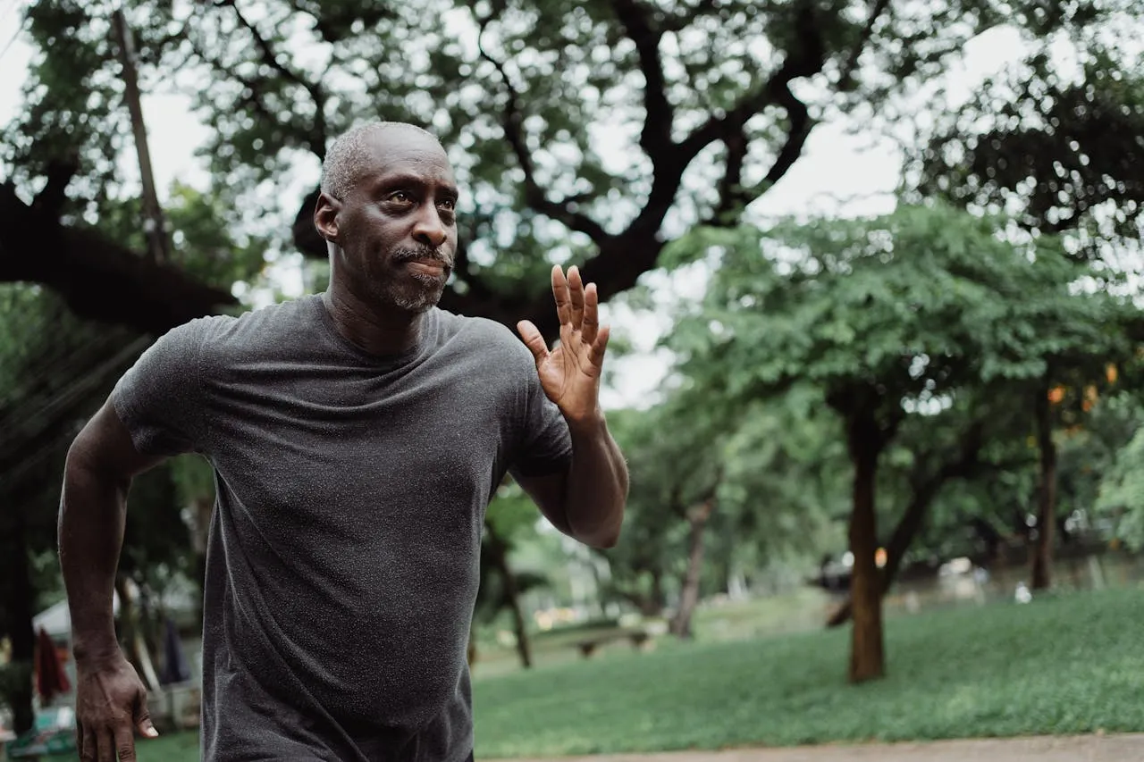 Middle-aged man jogging outdoors in a lush green park, focusing on fitness and a healthy lifestyle.