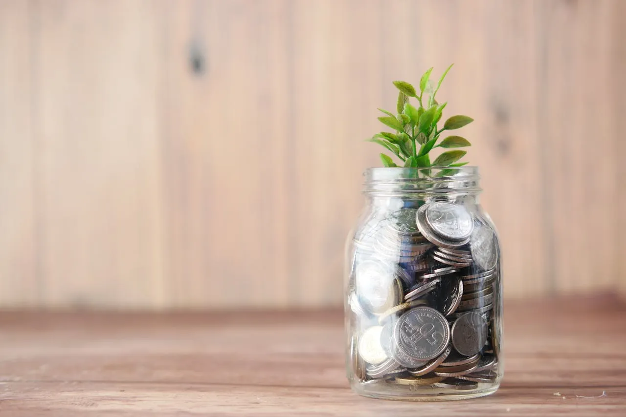 A glass jar filled with coins and a small green plant growing from the top, symbolizing financial growth and savings.