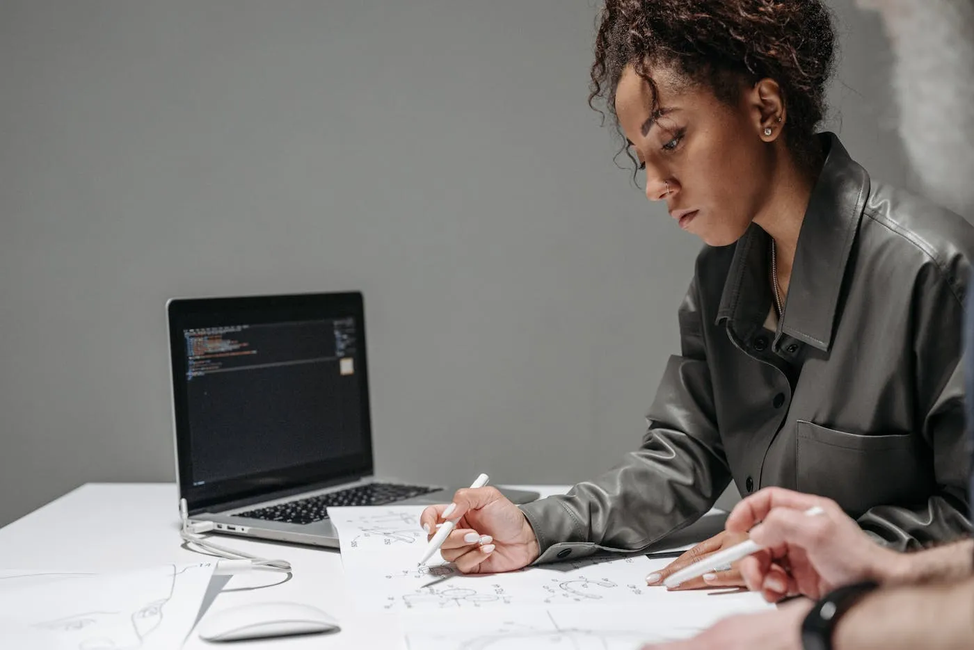 A focused software engineer sketching out system diagrams on paper, with a laptop displaying code in the background.