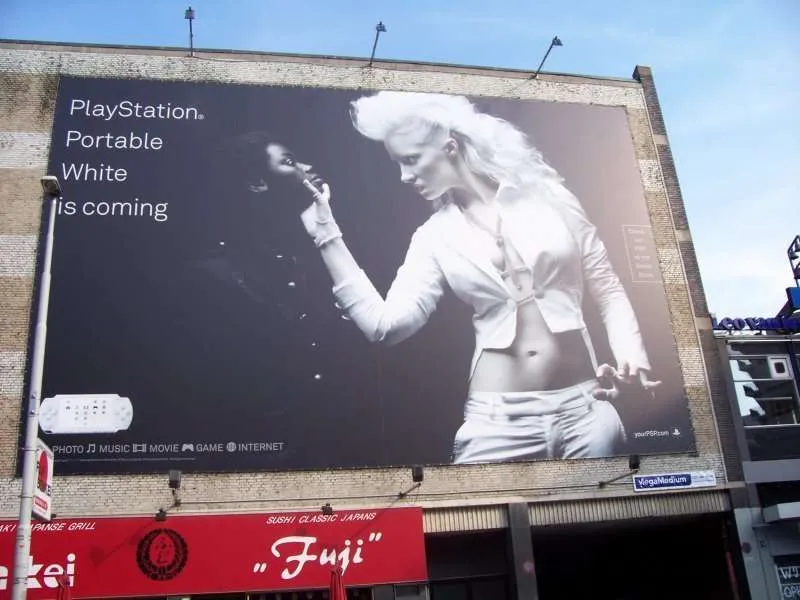 Controversial PlayStation Portable advertisement on a building, showing a white-clad woman touching the chin of a black-clad woman, with the text “PlayStation Portable White is coming.”
