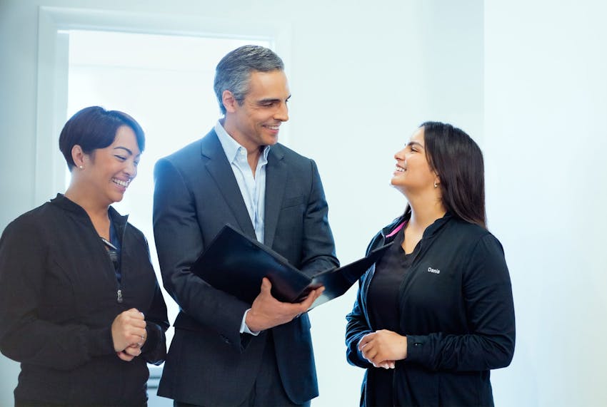 Anthony in suit holding binder with 2 of the female staff next to him