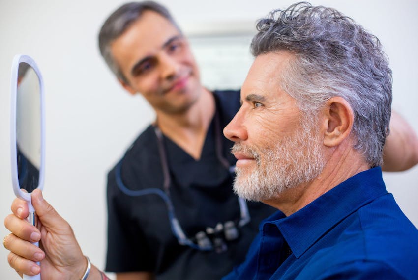 male client looking in handheld mirror at his beard
