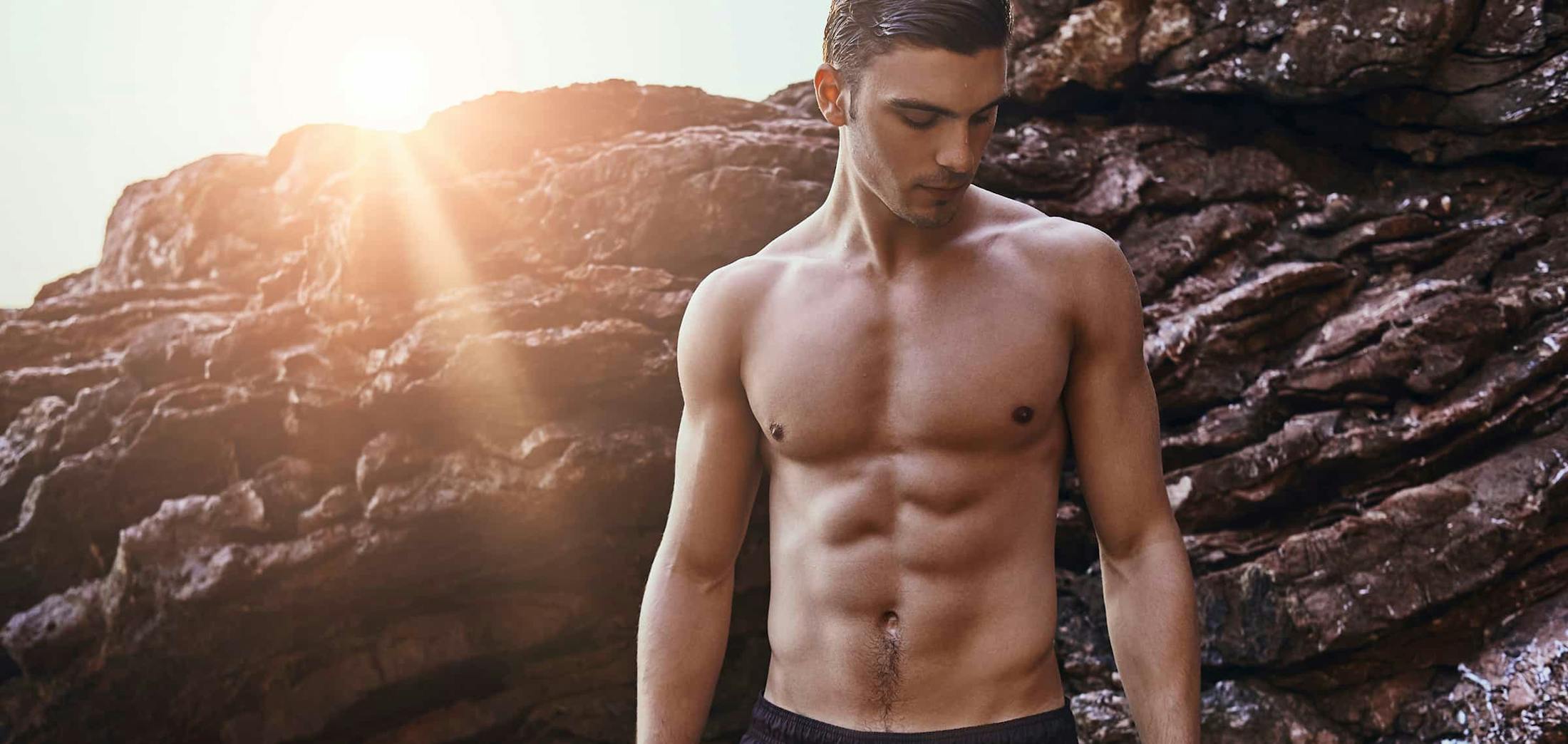 Shirtless man looking down, standing in front of rocks