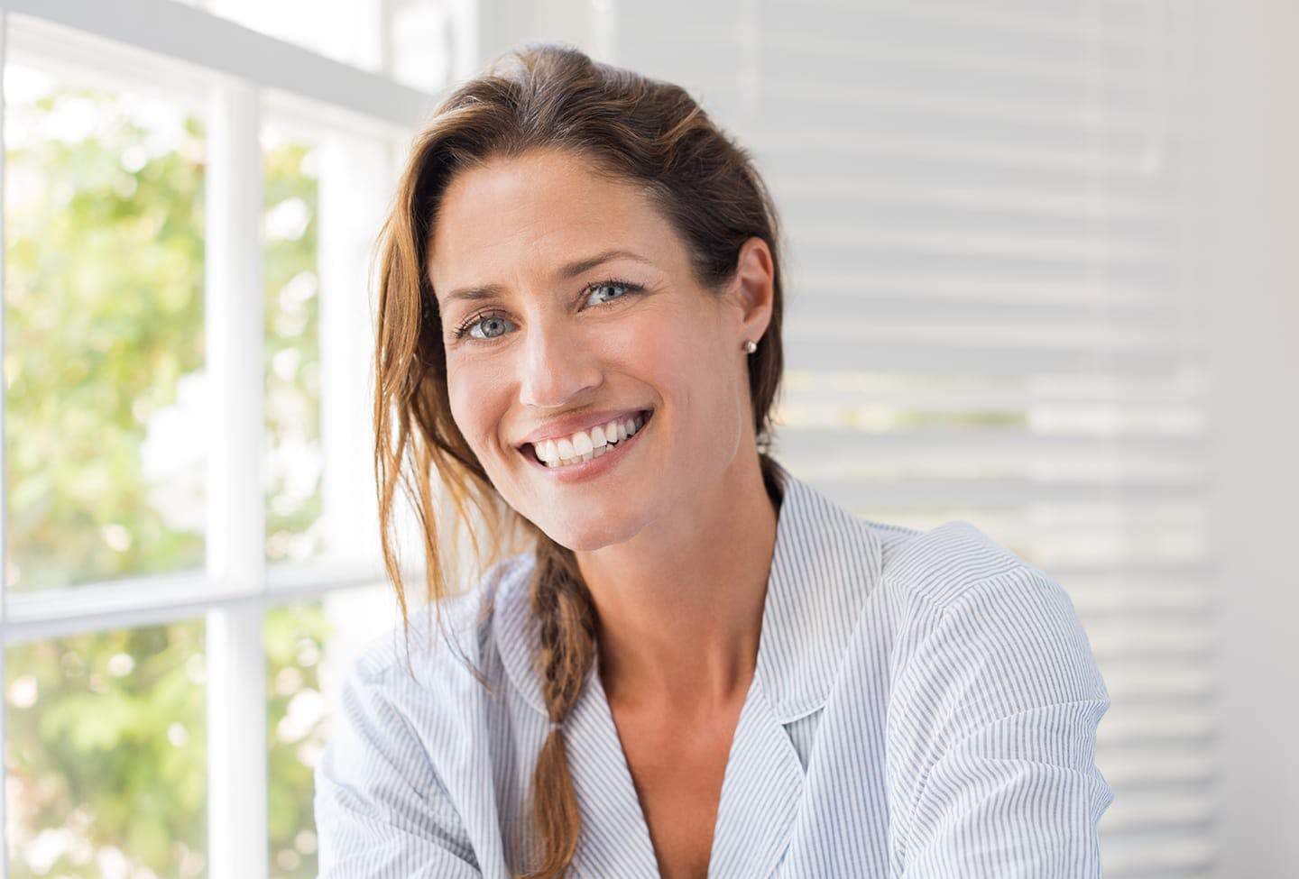 Model smiling big while sitting next to a window
