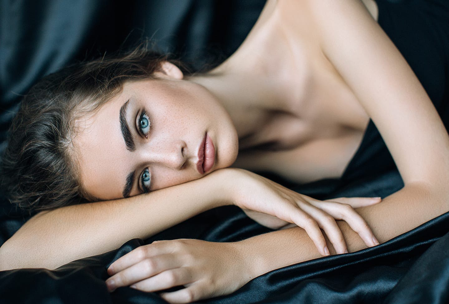 Model laying on a silk sheet resting her head against her arm