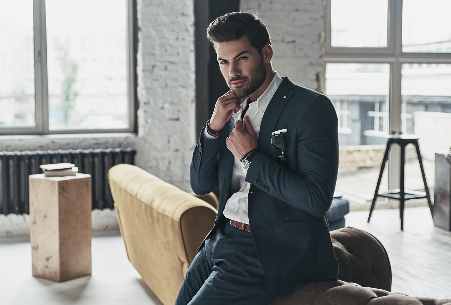 Man leaning against a couch while fixing his tie