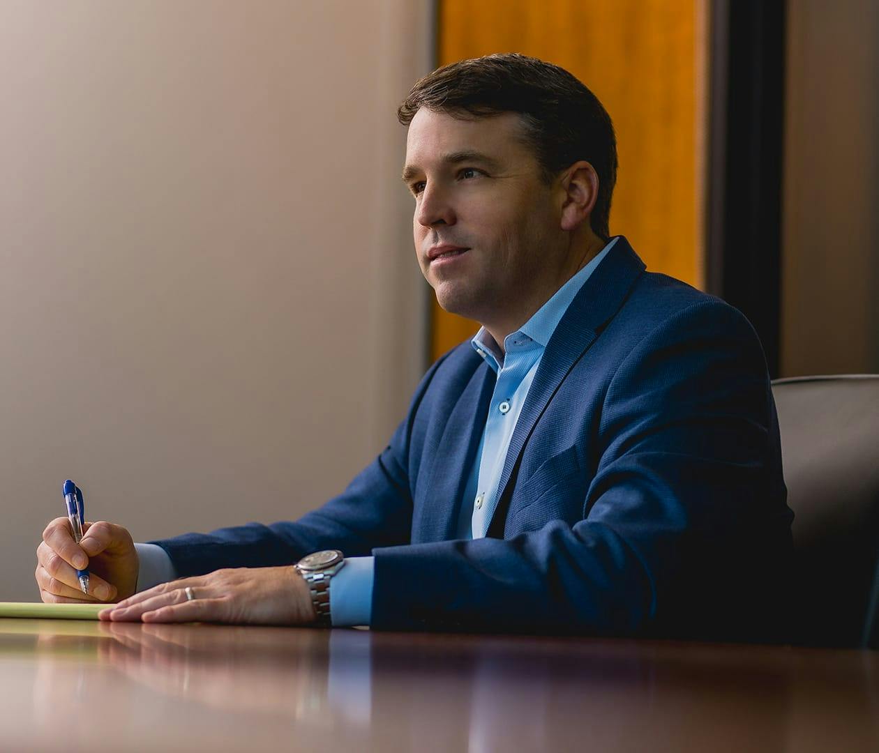 man sitting at table while in suit writing down notes