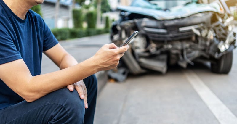 A person texting by a crashed car