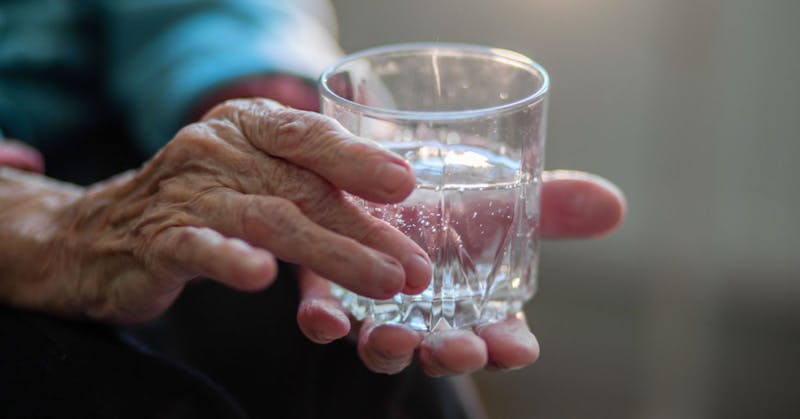 An older person holding a glass of water