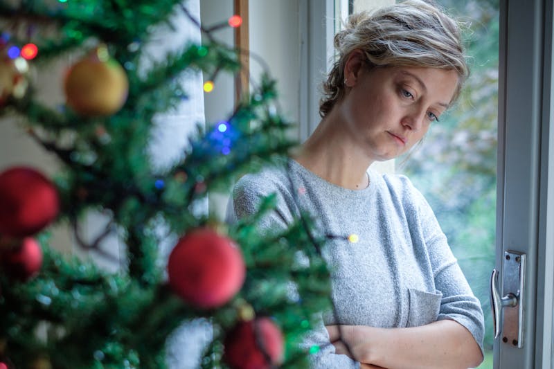 A sad woman standing by Christmas tree
