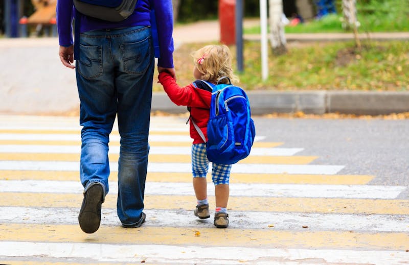 A child and adult holding hands walking across street