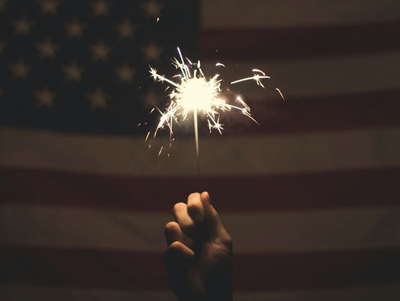 A person holding a sparkler in front of the flag