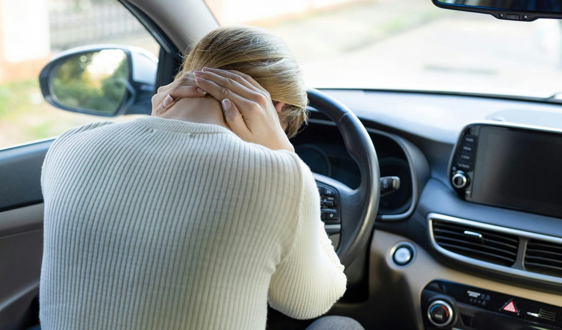 woman holding her neck in a car