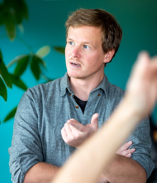 Man speaking and gesturing in conversation Man in gray shirt gesturing while speaking against turquoise background with plants