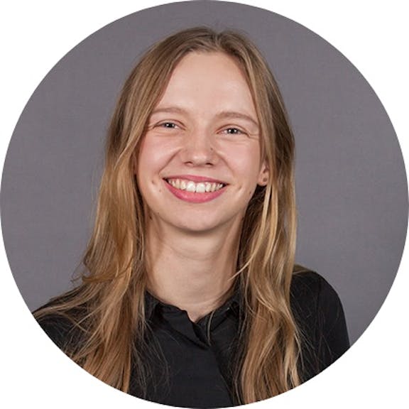 Portrait photo of a smiling woman with shoulder-length brown hair wearing a black shirt against a gray background