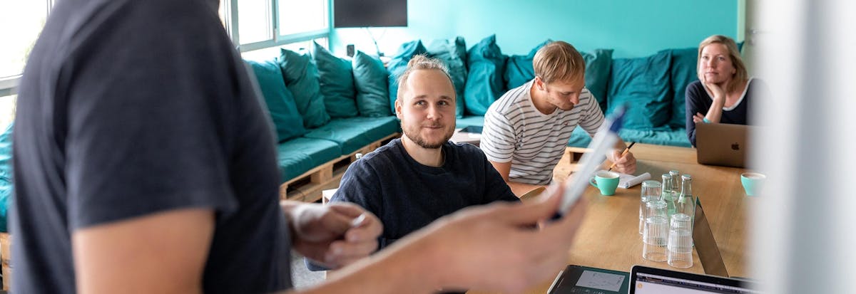 Group discussion during a workshop with multiple people gathered around a table in a bright room with a turquoise couch.