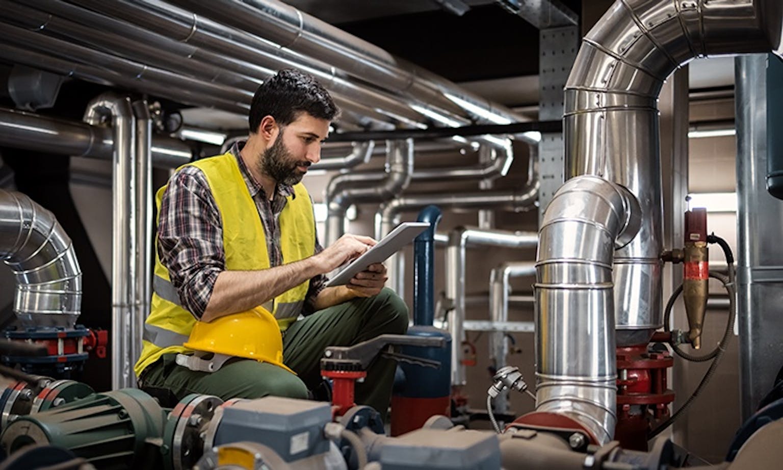 Wartung und Inspektion von Rohrleitungssystemen Techniker in Schutzweste inspiziert Rohrleitungssystem in Industrieanlage mit Tablet