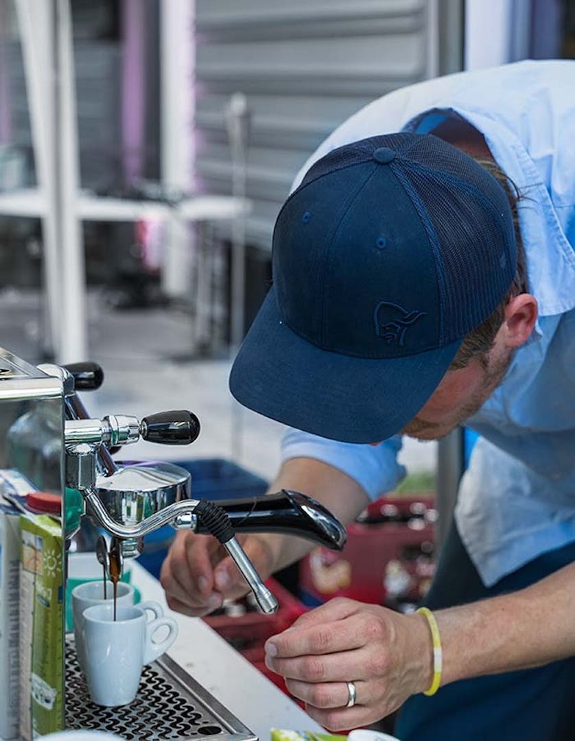 Man in light blue shirt and dark blue cap making coffee at a summer festival