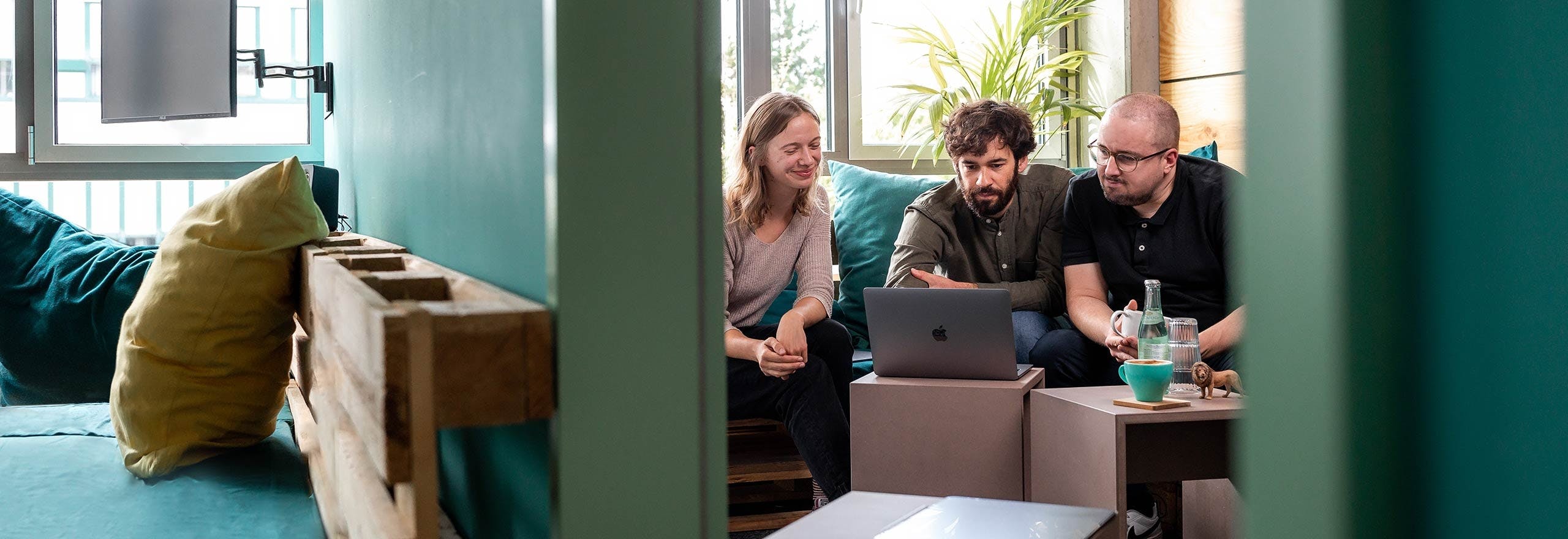Drei Personen sitzen zusammen auf einem Sofa und schauen auf einen Laptop-Bildschirm während einer Projektbesprechung.