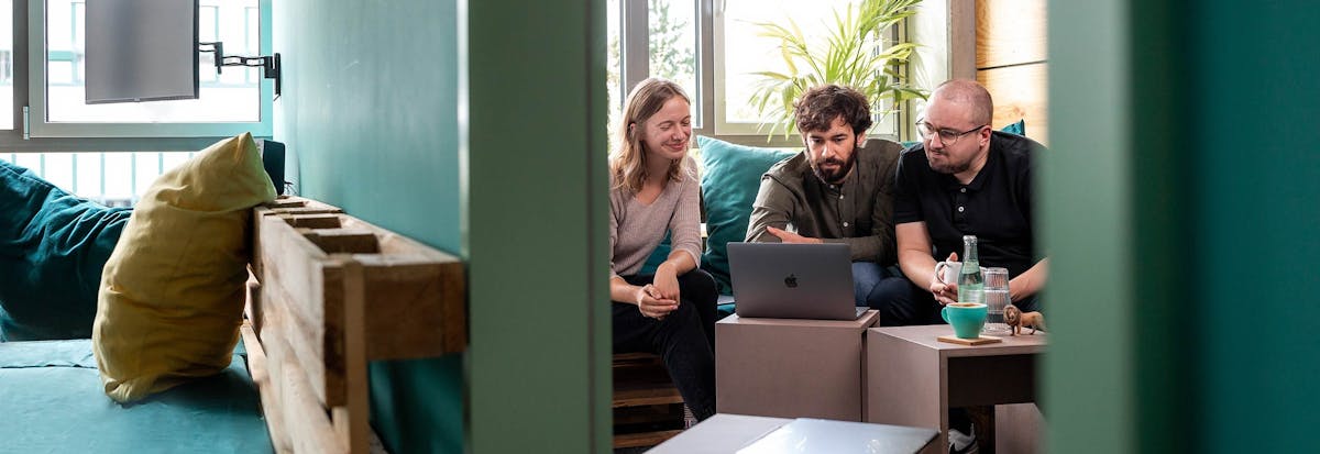 Three people sit together on a sofa reviewing a laptop screen during a project meeting.